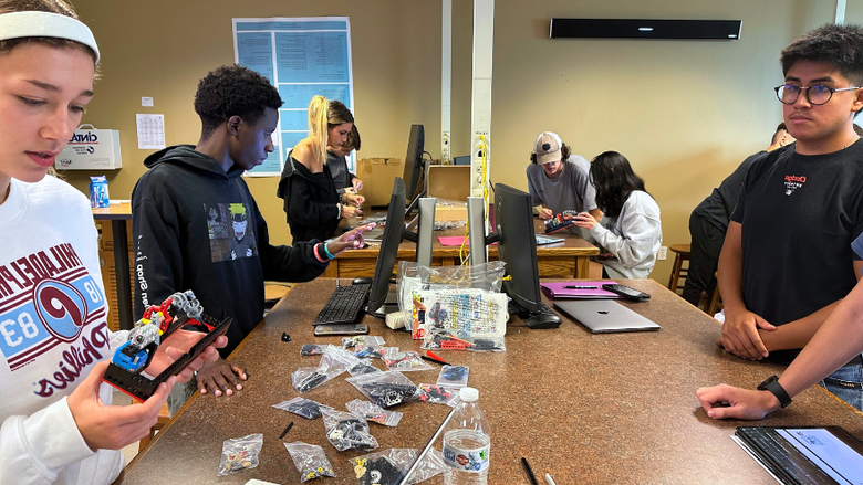 students working with computers and other STEM-related tools at a long desk