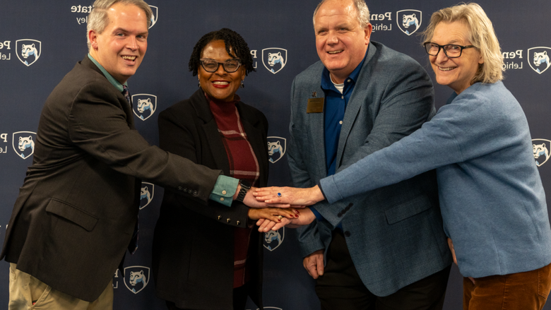 four individuals put their hands in a pile in the middle and smile at the camera 